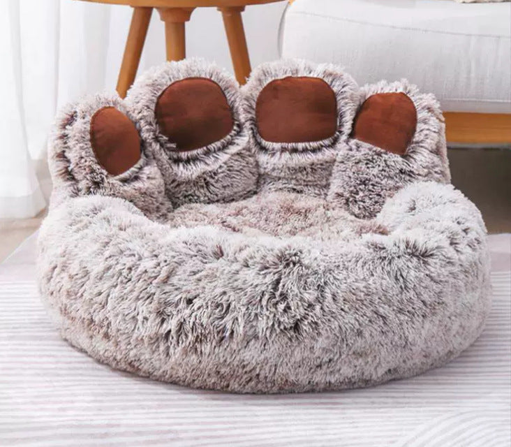 Warm coffee plush paw pet bed beside a wooden stool in a bright room