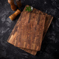 Two end-grain teak cutting boards stacked on a dark stone counter