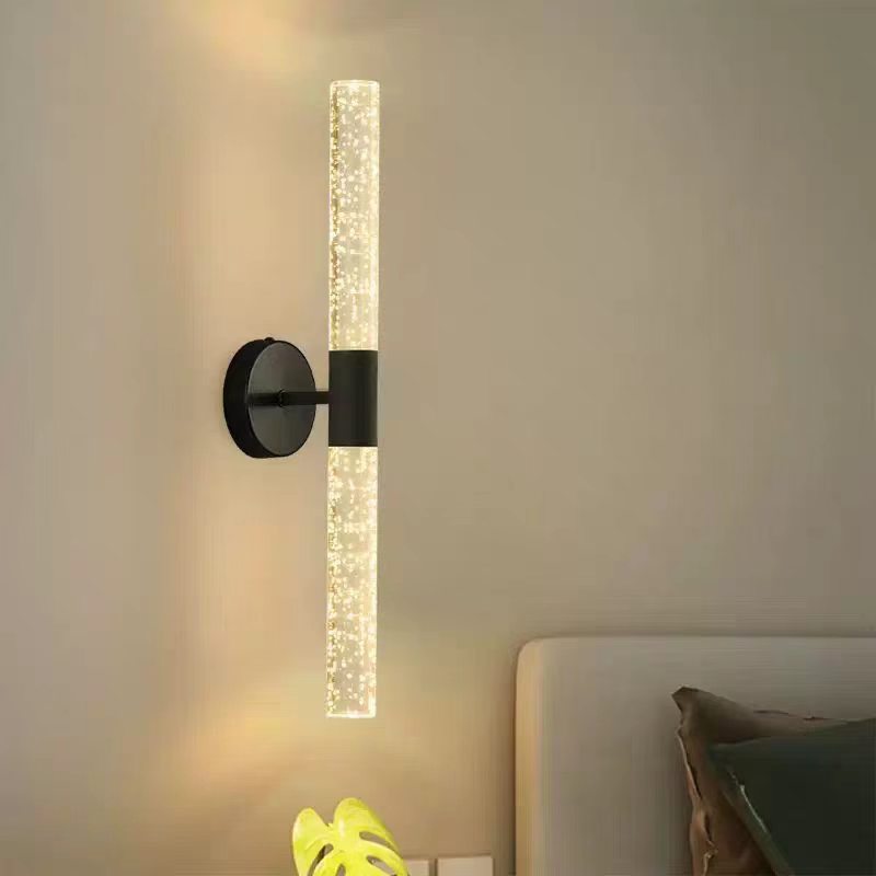 Black wall sconce lit beside a bed