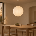 Paper globe pendant glowing above a pale oak dining table